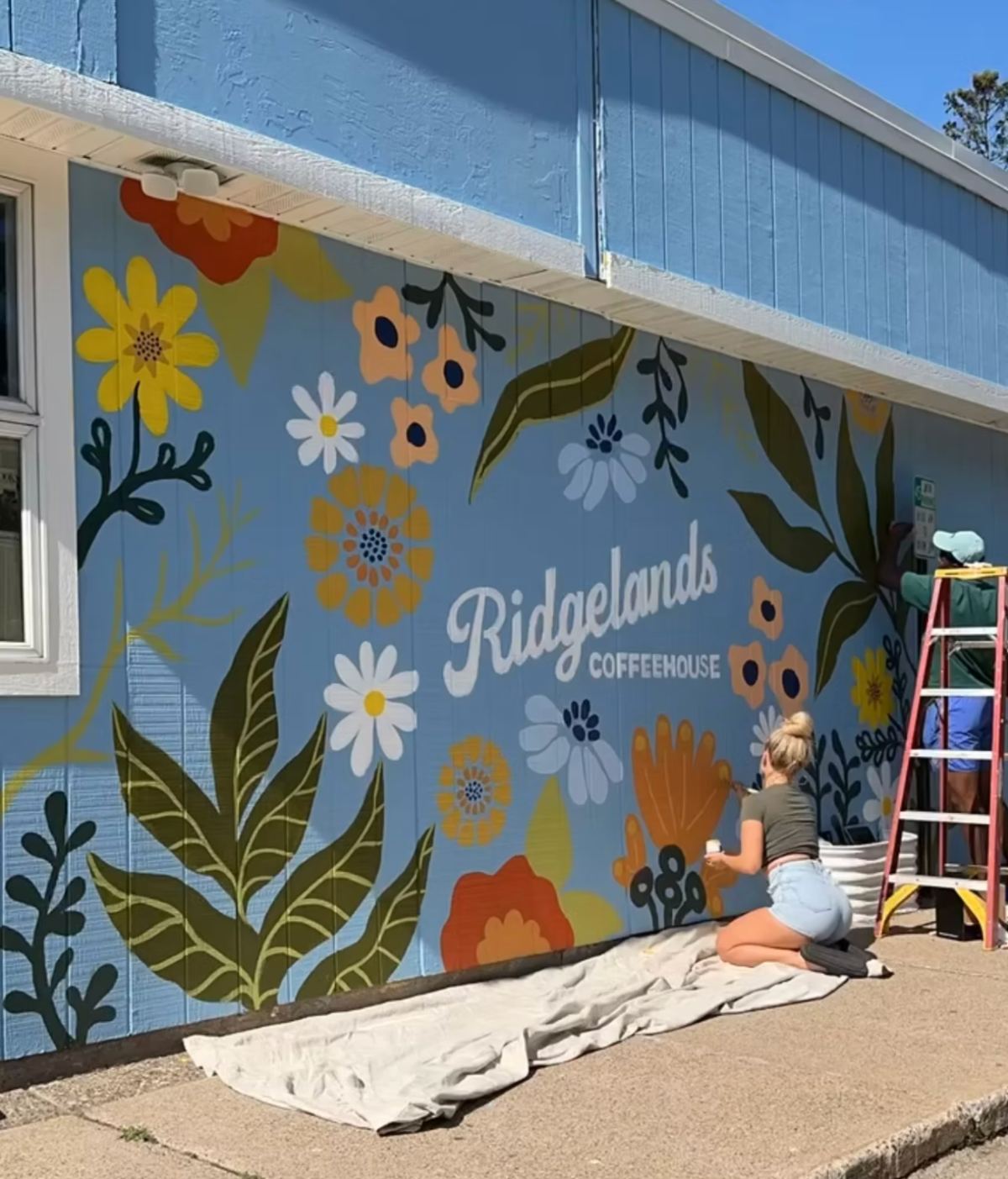 Blue exterior wall covered in large painted flowers with Ridgelands Coffeehouse lettering — hand-painted mural in Winona, Minnesota by Scout Hill Co